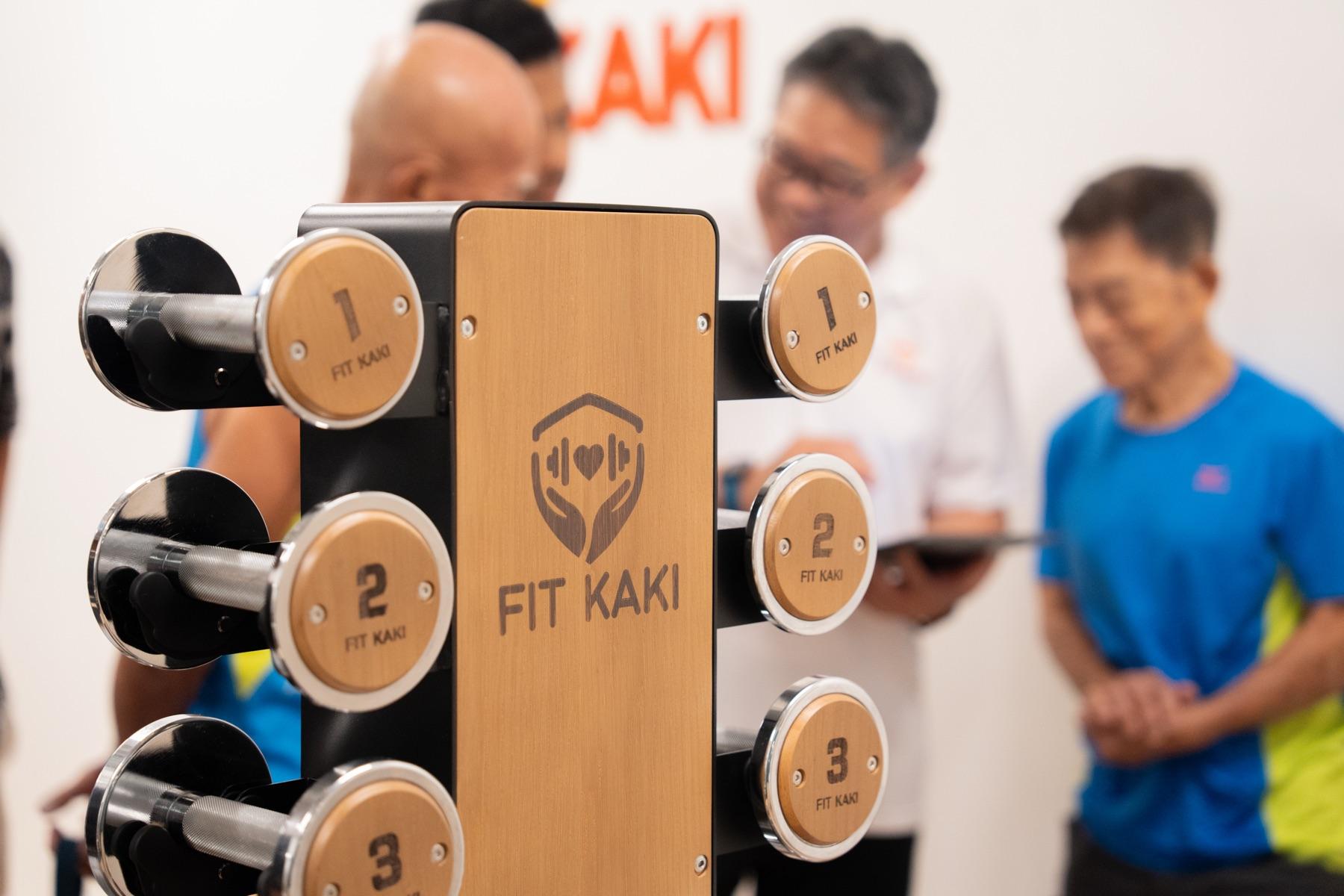 Fit Kaki's wooden dumbbell rack in the bright Eunos studio, with a small group session in the background